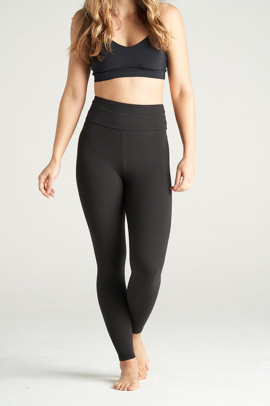 Woman standing in a relaxed pose wearing black high-waisted full-length leggings and a black sports bra, showcasing activewear against a neutral background