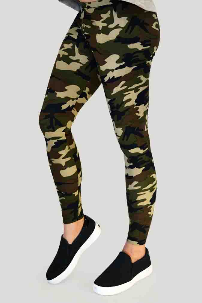 Woman modeling high-waisted green camouflage leggings, barefoot in a neutral indoor studio. The leggings feature an earthy camo pattern in shades of olive, brown, and khaki, paired with a black sports bra for a sporty and confident look. Ideal for gym, yoga, or casual streetwear.