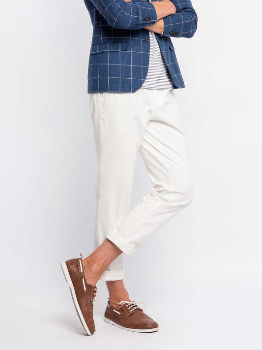 Man standing with legs crossed, wearing brown leather loafers and white cuffed trousers with hidden loafer liner socks, styled for smart casual or business casual summer outfits