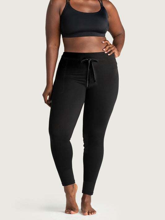Plus size black lounge leggings for women with drawstring waist and side pockets, shown on barefoot model in studio, perfect for casual wear, yoga, or loungewear.