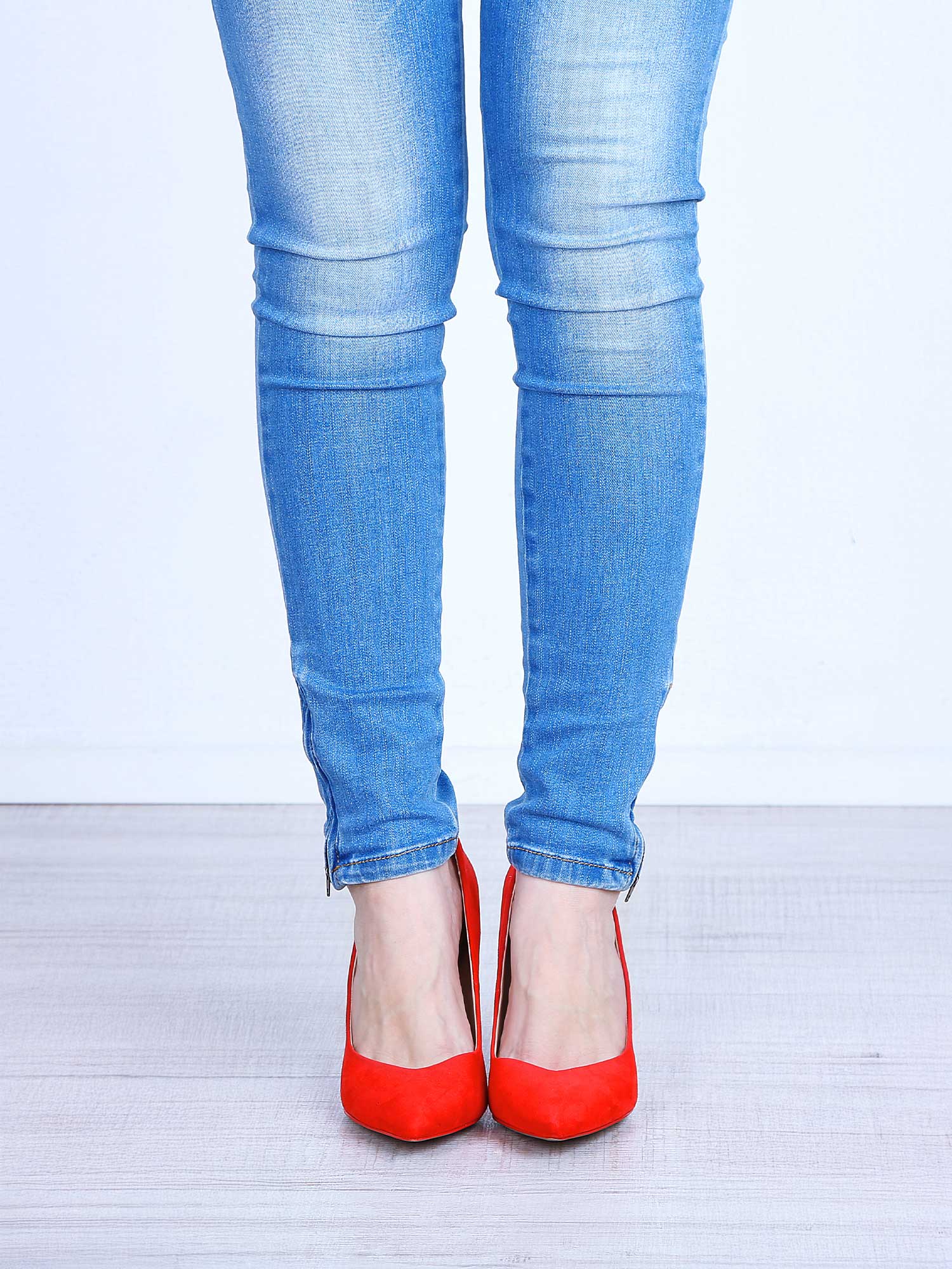 Blue jeans worn with red shoes on a light background