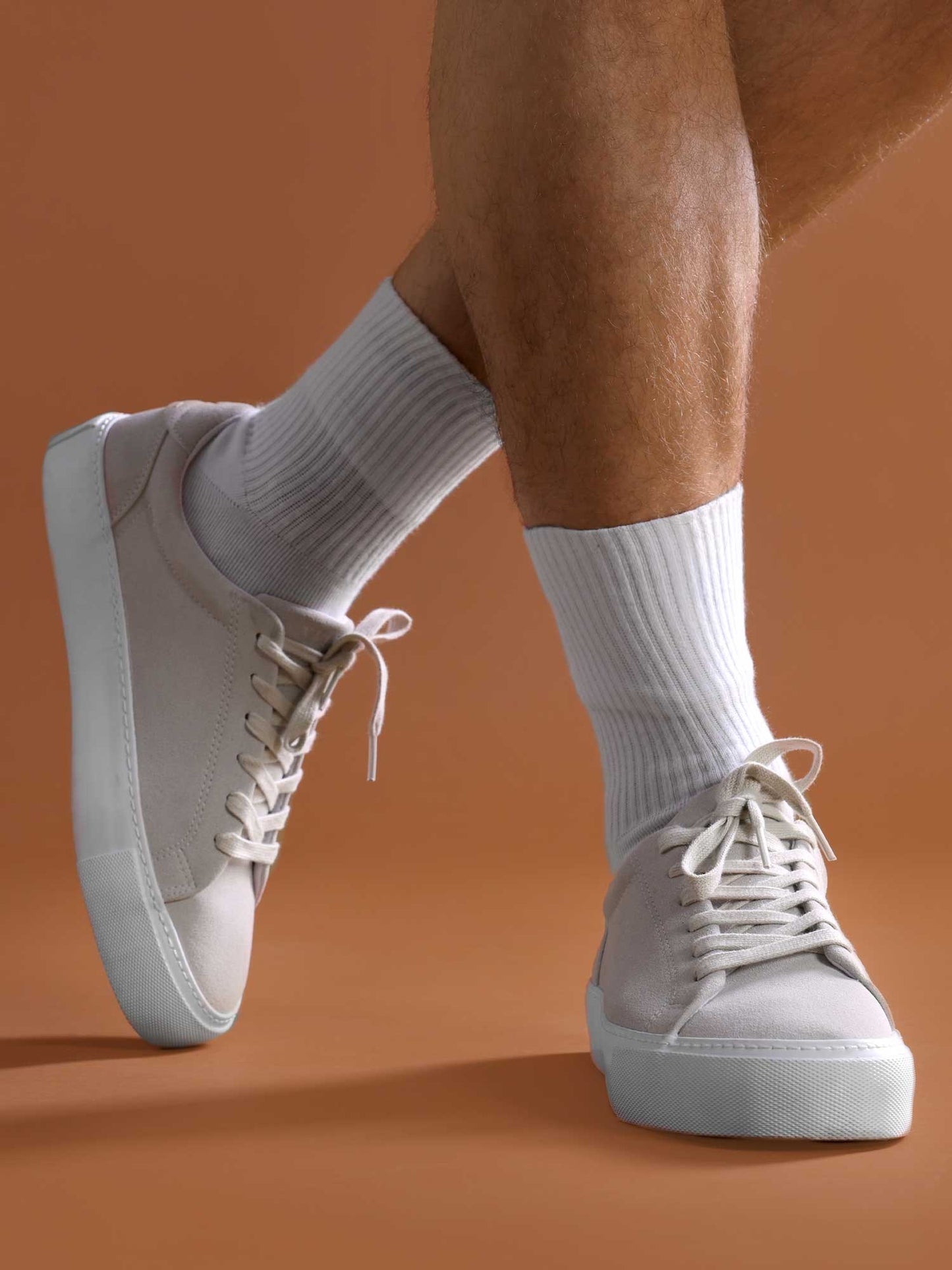 Man posing with one leg crossed, wearing white ribbed crew socks and beige low-top sneakers, styled for casual everyday wear or athleisure fashion