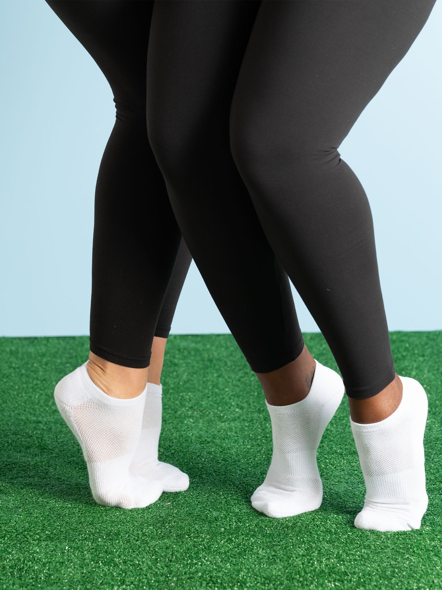 Two pairs of black leggings worn by people on a grassy surface with a light blue sky.