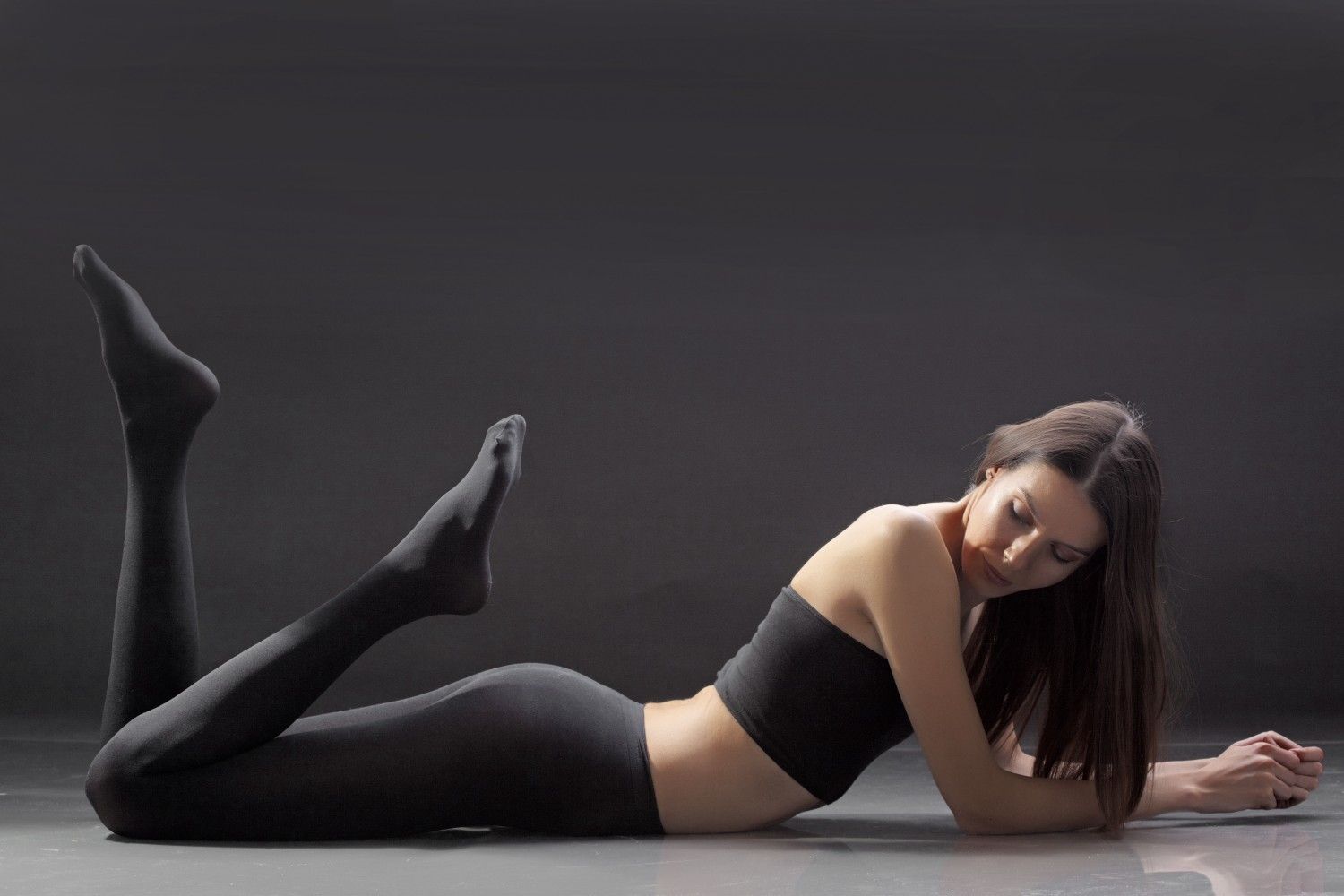 Woman in black athletic legging tights wear lying on a dark surface