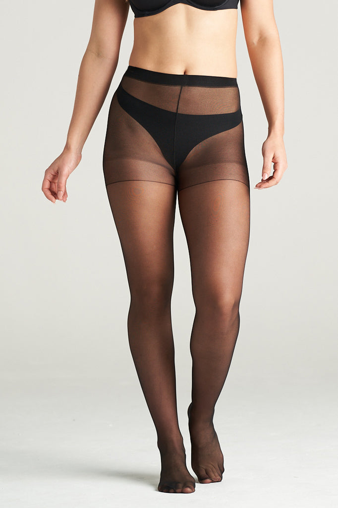 Woman modeling light support sheer hosiery in black tone, standing in a graceful front pose with one leg lifted, showcasing the smooth, semi-transparent finish and high-waisted support band