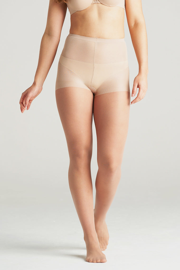 Woman modeling nude light support sheer hosiery, standing barefoot with one leg slightly forward and arms relaxed, showcasing the smooth high-waisted design and comfortable compression fit for everyday wear under skirts or dresses.