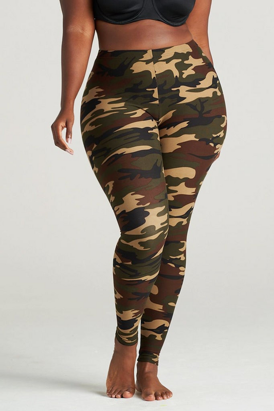 Plus Size Woman modeling high-waisted green camouflage leggings, barefoot in a neutral indoor studio. The leggings feature an earthy camo pattern in shades of olive, brown, and khaki, paired with a black sports bra for a sporty and confident look. Ideal for gym, yoga, or casual streetwear.