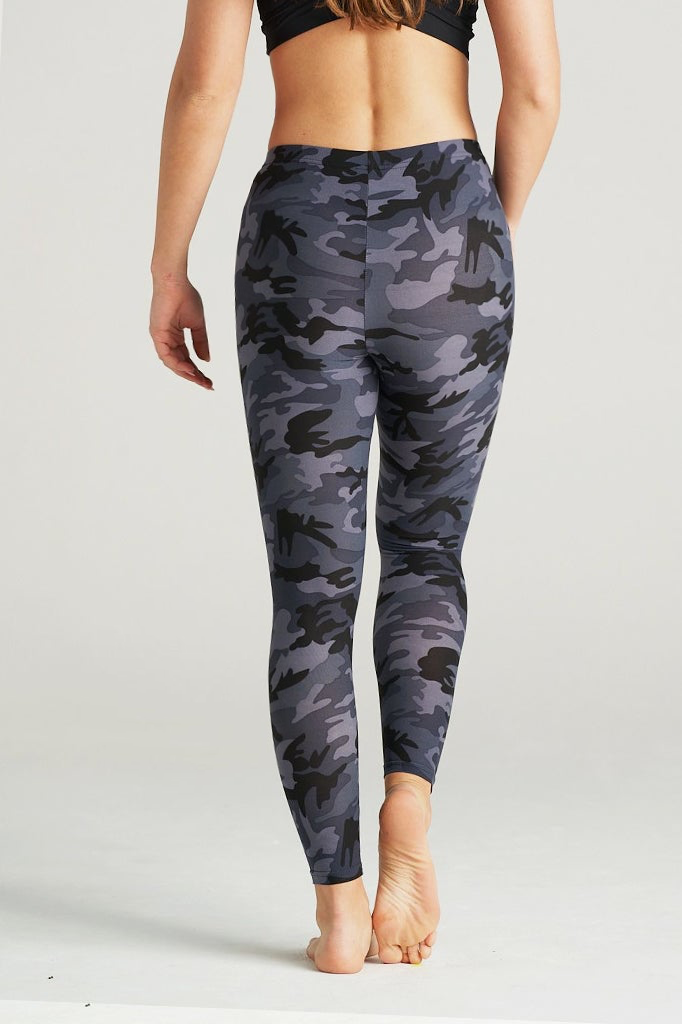 Woman wearing high-rise grey camouflage leggings with a sleek fit, paired with a black sports bra. She stands barefoot on a neutral studio backdrop, showcasing the leggings' bold grey, black, and charcoal camo pattern. Ideal for fitness, yoga, and everyday activewear.