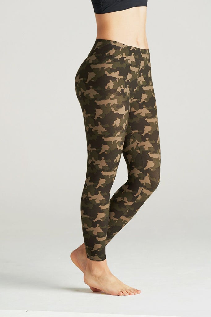 Woman modeling high-waisted green camouflage leggings, barefoot in a neutral indoor studio. The leggings feature an earthy camo pattern in shades of olive, brown, and khaki, paired with a black sports bra for a sporty and confident look. Ideal for gym, yoga, or casual streetwear.