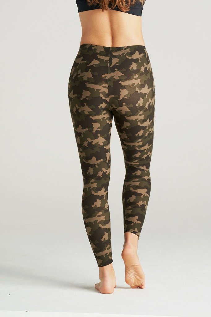Woman modeling high-waisted green camouflage leggings, barefoot in a neutral indoor studio. The leggings feature an earthy camo pattern in shades of olive, brown, and khaki, paired with a black sports bra for a sporty and confident look. Ideal for gym, yoga, or casual streetwear.