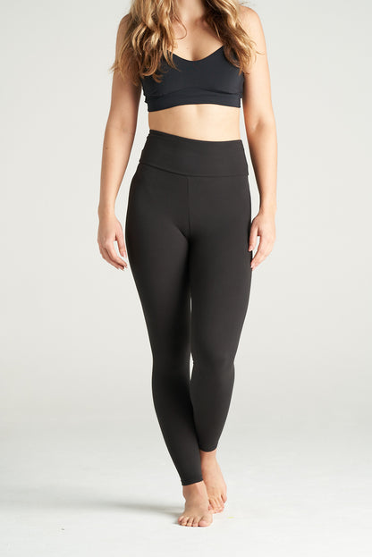 Woman standing in a relaxed pose wearing black high-waisted full-length leggings and a black sports bra, showcasing activewear against a neutral background.