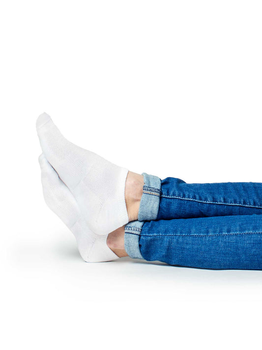 Person lying down with legs extended, wearing white low-cut athletic socks and rolled cuff blue jeans, showcasing breathable cotton socks ideal for everyday wear, walking, or light workouts