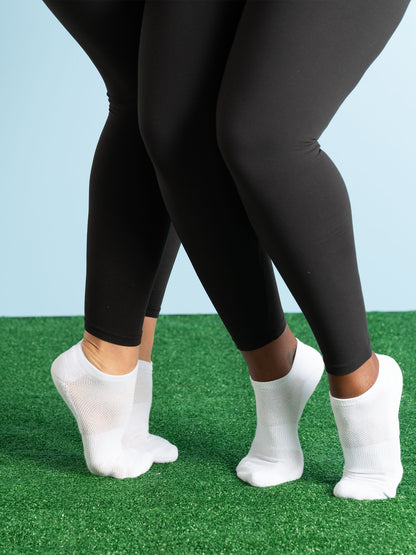 Two pairs of black leggings worn by people on a grassy surface with a light blue sky.